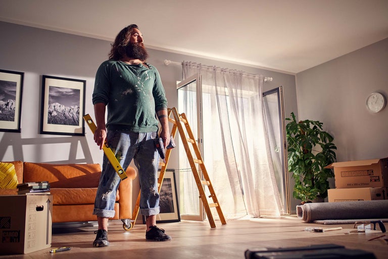 Pièce lumineuse en cours de rénovation avec artisan, niveau à bulle, échelle et cartons de déménagement