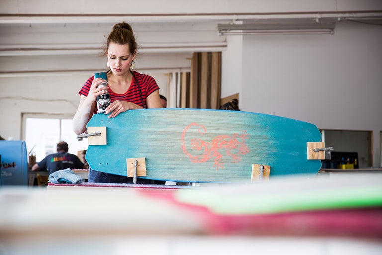 Une femme travaille une planche en bois bleue avec une fraiseuse dans un atelier