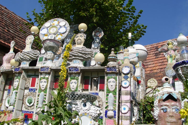 Vue détaillée d'une clôture de jardin créative avec des mosaïques, de la céramique et des sculptures.
