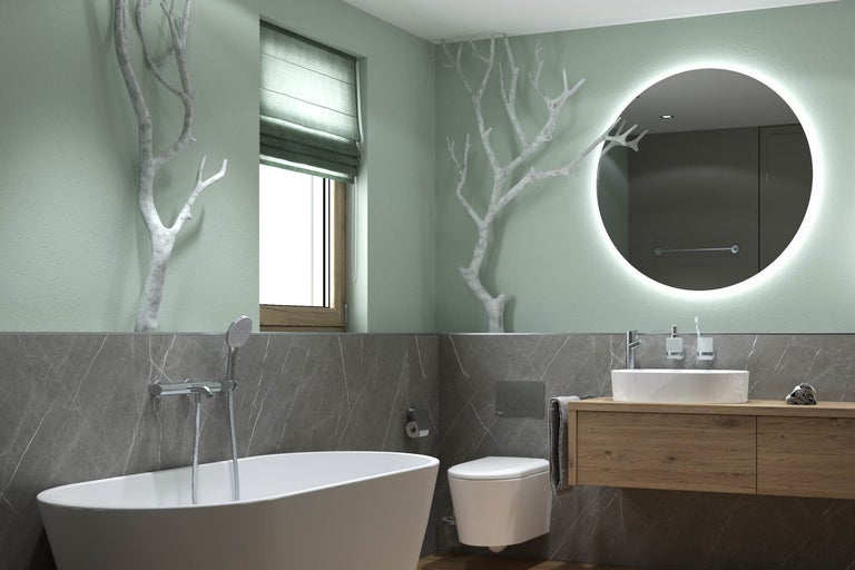 Salle de bains moderne avec baignoire en îlot, toilettes suspendues et meuble sous-vasque en bois. Grand miroir rond rétroéclairé et branches décoratives.
