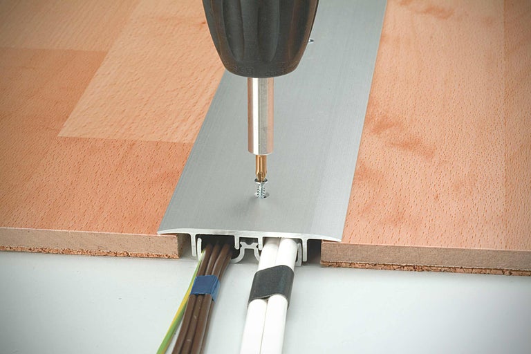 Fixation d'une plinthe de protection de câbles en aluminium sur un plancher en bois avec un tournevis