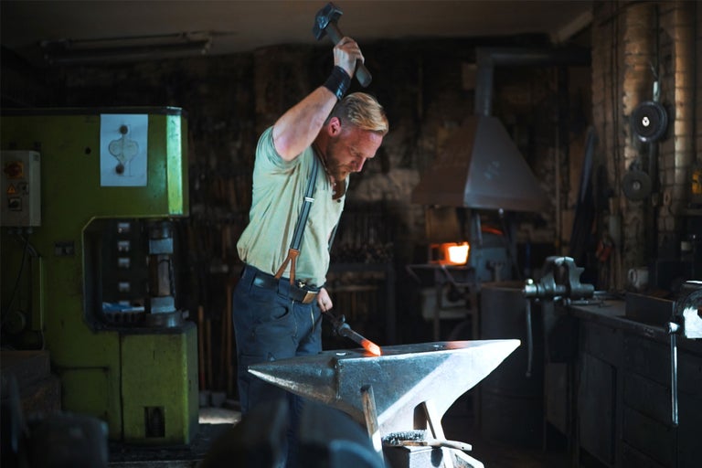 Schmied bei der Arbeit mit Hammer und Amboss in einer Werkstatt.