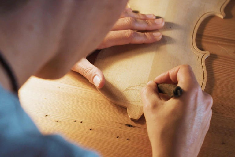 Eine Person zeichnet ein Muster auf ein hölzernes Geigenoberteil.