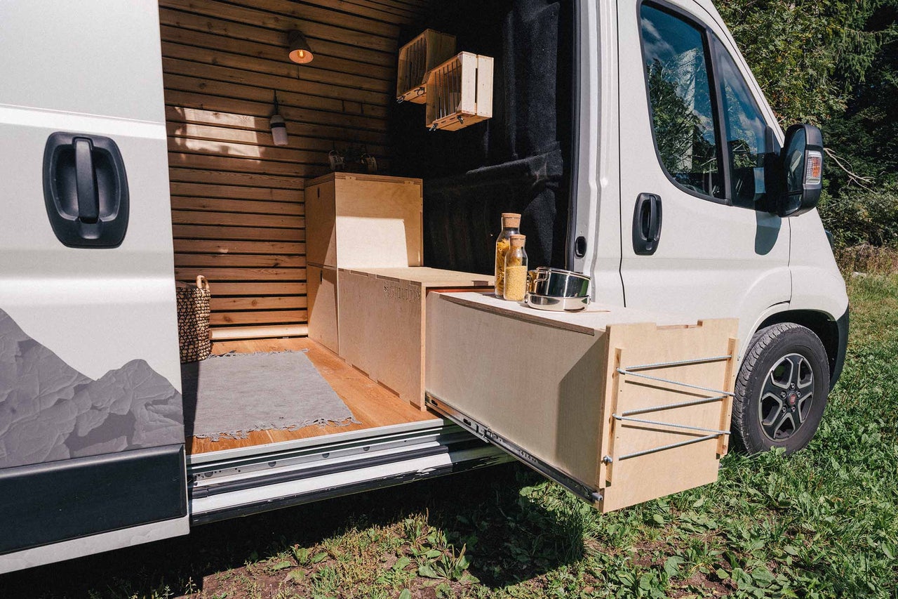 Intérieur d'un van aménagé avec revêtement en bois, tiroir de cuisine et provisions
