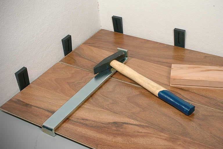 Verlegung von Laminat mit Hammer, Zugeisen und Abstandskeilen