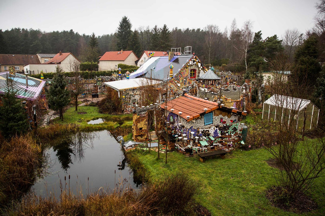 Vue d'un jardin avec un étang et une maison décorée de mosaïques et d'ornements.