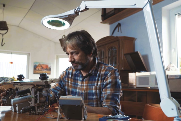 Ein Mann repariert mit einer Lupenleuchte elektronische Bauteile.