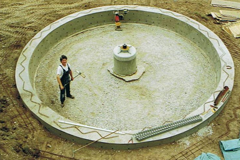 Chantier avec fondation ronde en béton, personne et matériel de construction.