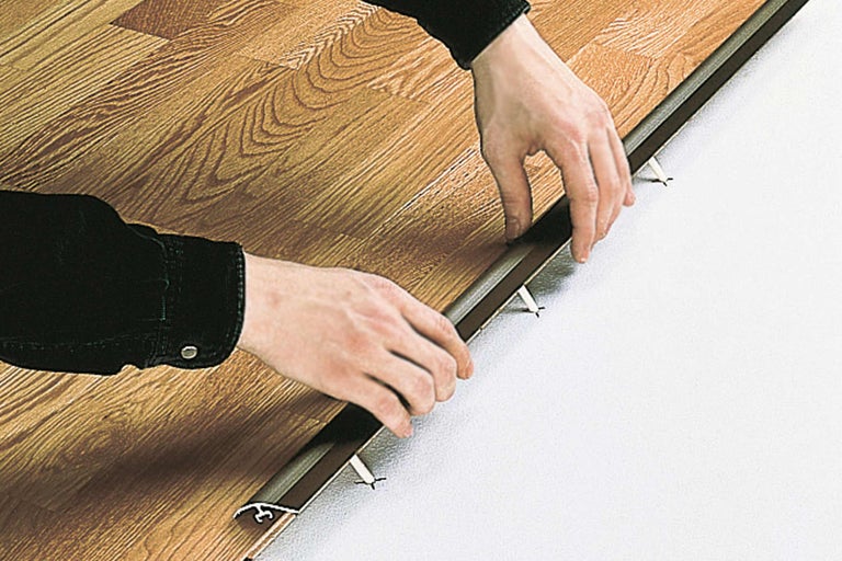 Un poseur de revêtements de sol installe un profilé de transition sur un plancher en bois
