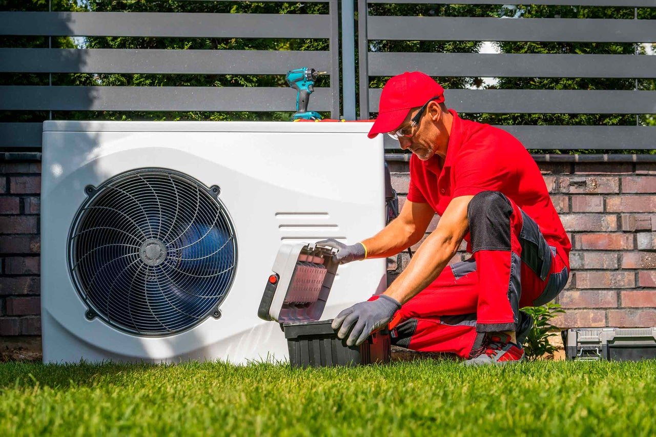 Ein Techniker wartet eine Wärmepumpe im Garten mit Werkzeugkasten