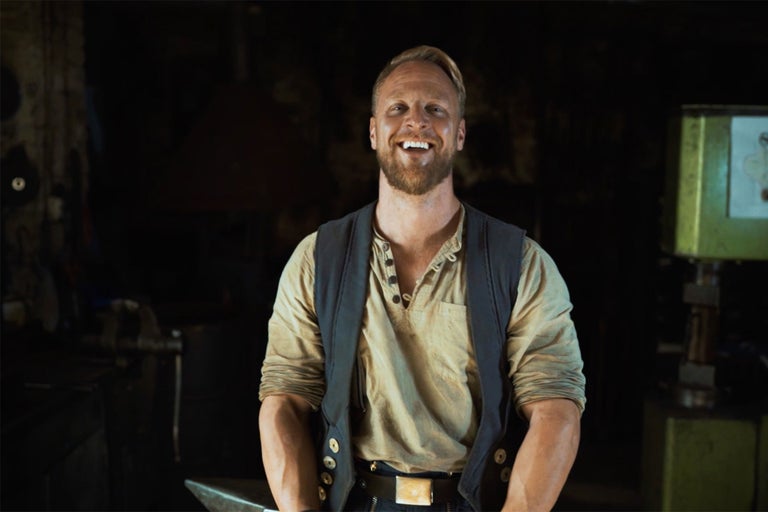 Lachender Mann mit Bart, Weste und Hemd in einer Werkstatt