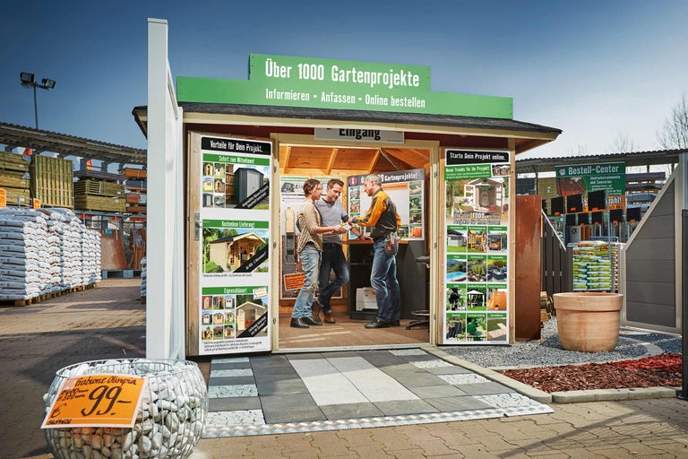 Aussenansicht eines Informationsstandes für Gartenprojekte mit zwei Kunden und einem Verkäufer