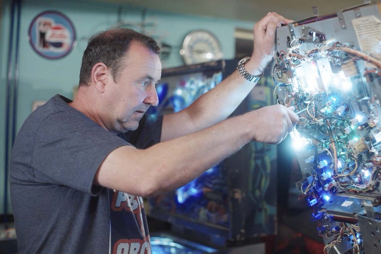 Ein Mann repariert einen Flipperautomaten mit Drähten und Lampen.