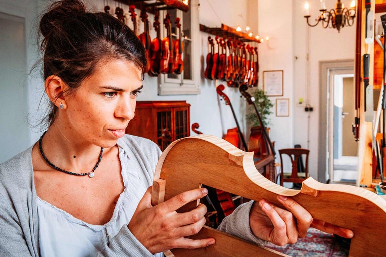 Une femme tient une caisse de violon inachevée dans un atelier