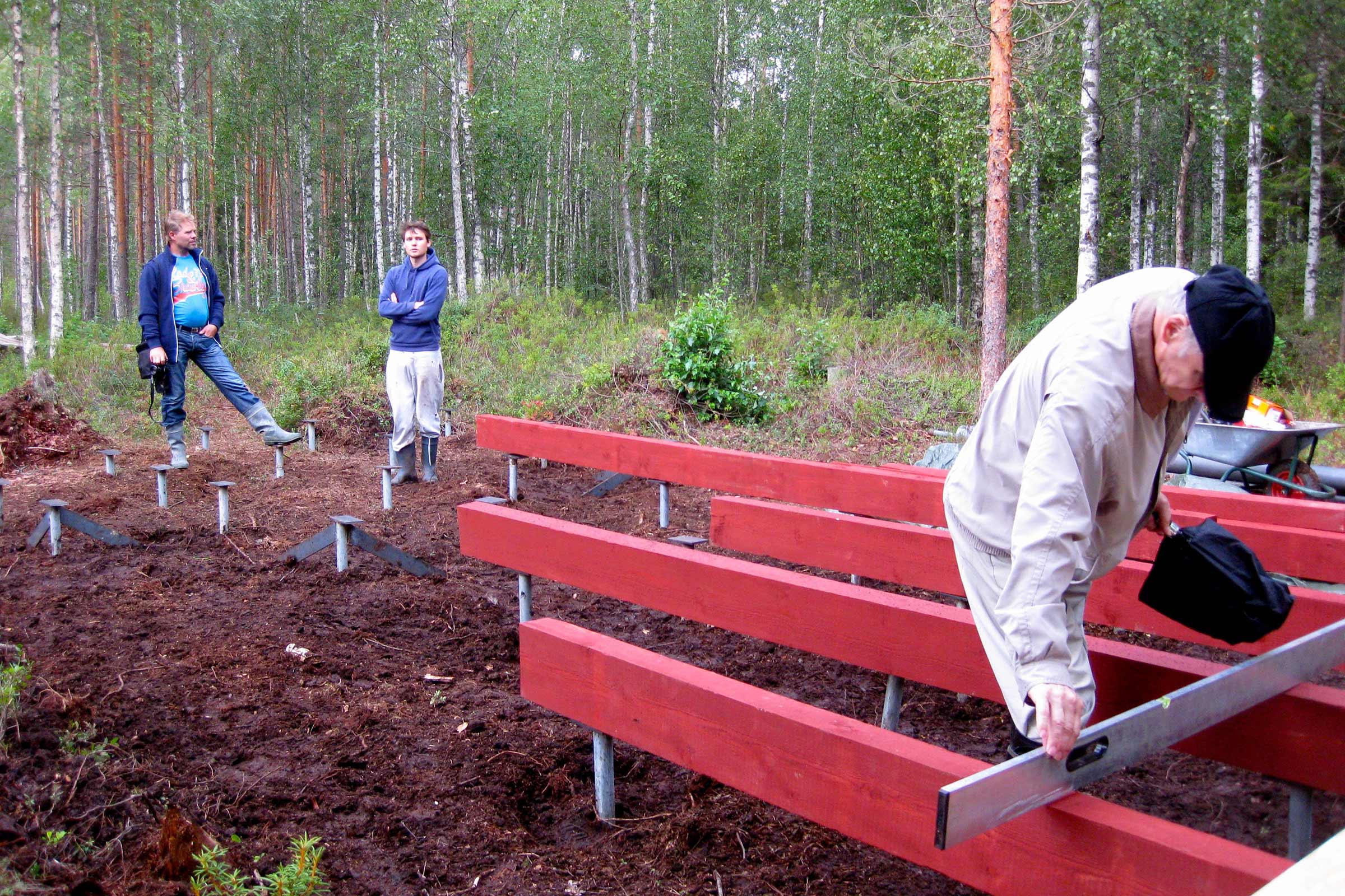 Trois personnes construisent des fondations en bois et poteaux métalliques dans la forêt.