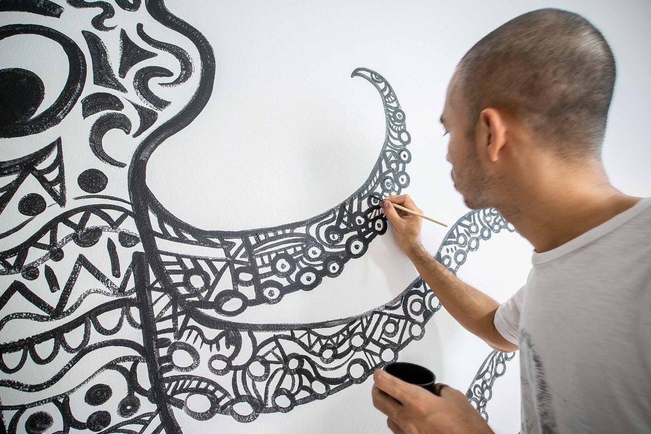 Ein Künstler malt mit einem Pinsel ein abstraktes Muster auf eine Wand.