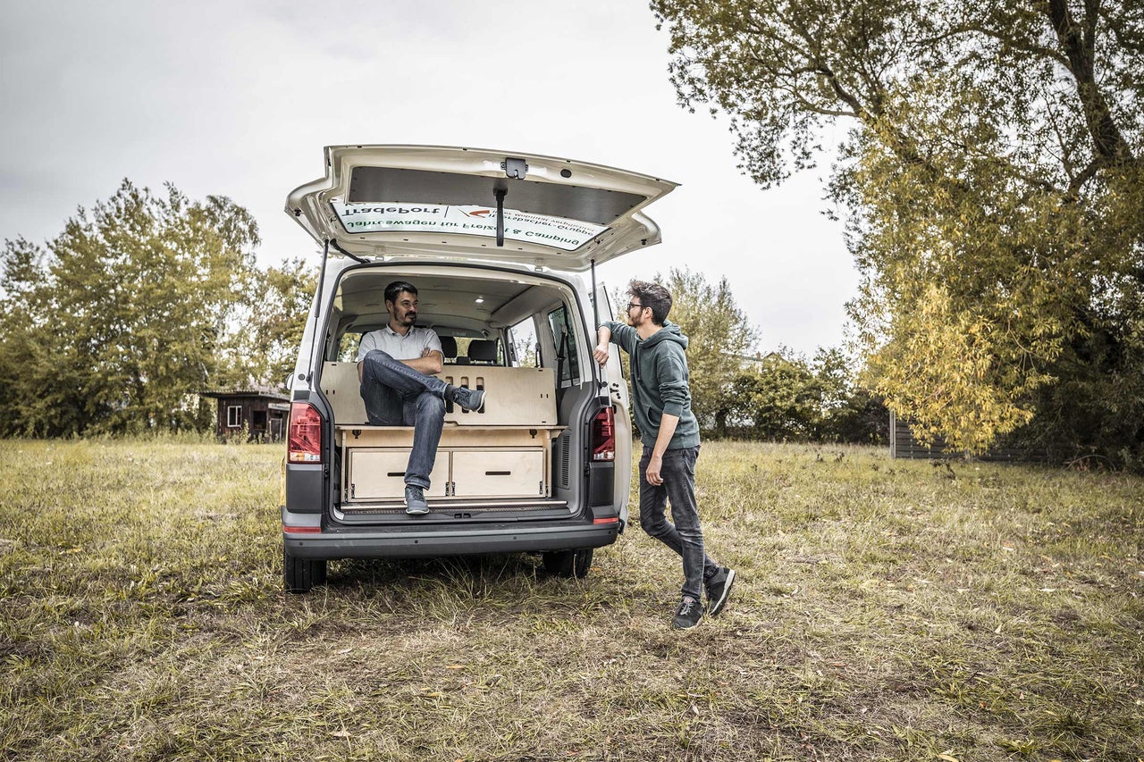 Deux hommes près d'un van transformé avec aménagement en bois et tiroirs dans un pré.