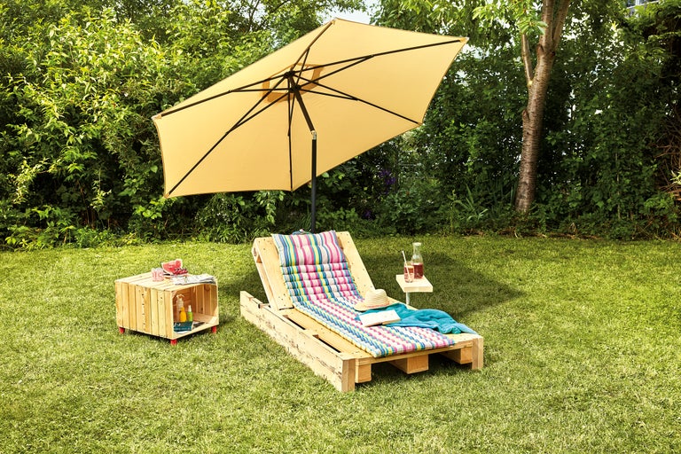 Scène de jardin avec parasol, chaise longue en palettes de bois et table d'appoint