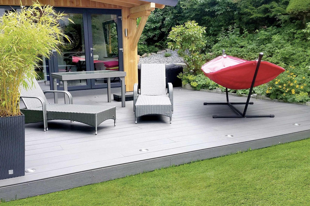 Terrasse mit Gartenmöbeln, einschließlich Stühlen, Tisch und Hängematte, umgeben von Pflanzen und Rasen.