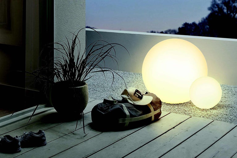 Scène de terrasse décorative avec deux lampes sphériques d'extérieur, une plante en pot et un sac de voyage avec une casquette