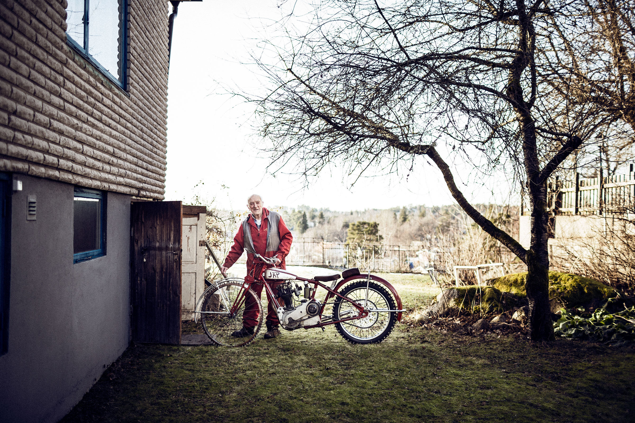 Ein Mann steht neben einem Oldtimer-Motorrad vor einem Haus auf einem Rasen