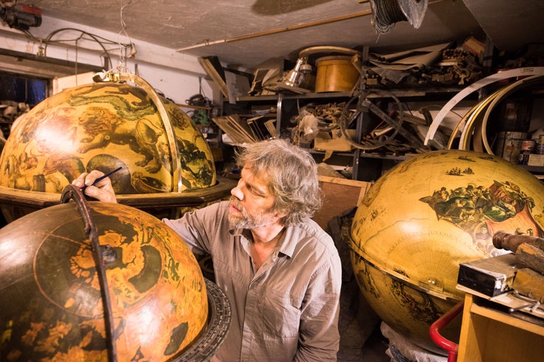 Un homme restaure un globe dans un atelier.