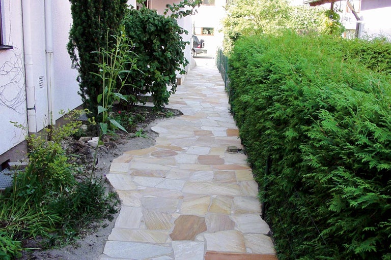 Chemin de jardin en dalles de pierre naturelle avec plantes vertes adjacentes