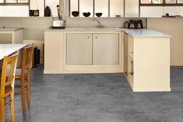 Cuisine avec revêtement de sol gris aspect carrelage, kitchenette et chaises.