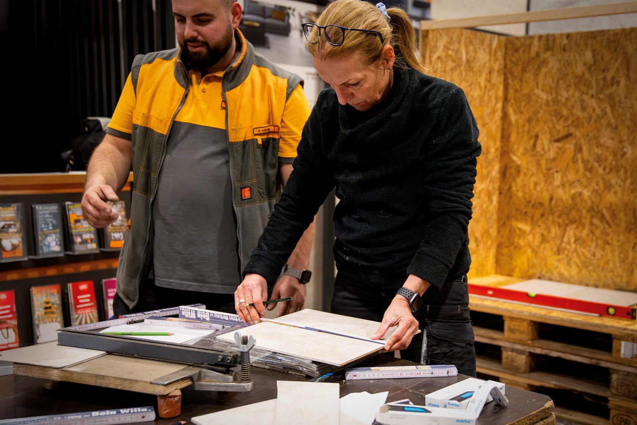 Deux personnes mesurent un carreau avec un crayon et une règle sur une table avec des outils.