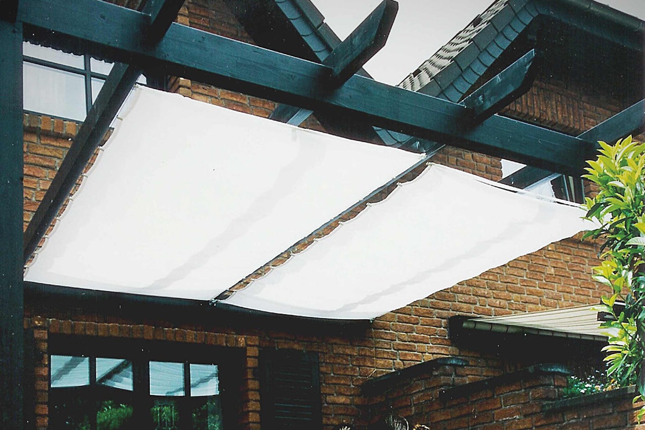 Pergola mit weissem Sonnensegel vor einem Backsteingebäude
