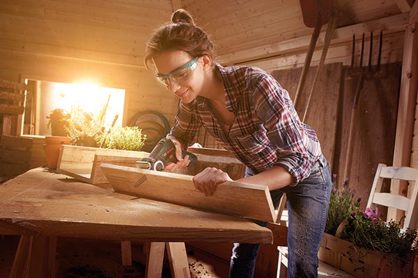 Frau arbeitet mit einem Multifunktionswerkzeug an einem Holzstück in einer Werkstatt.