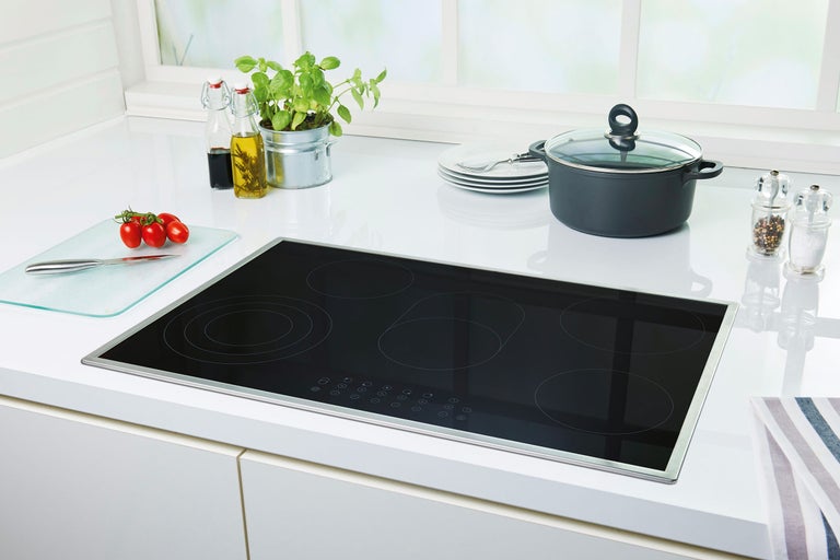 Table de cuisson à induction noire avec cinq zones de cuisson sur un comptoir de cuisine.