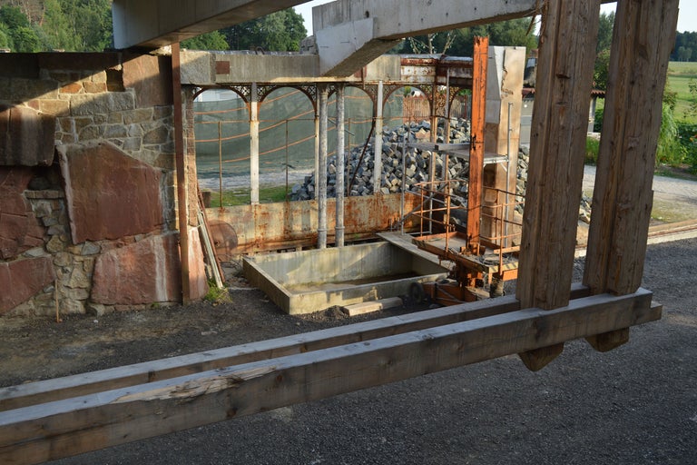 Vue d'un chantier avec mur en pierre, structures en béton et poutres en bois.