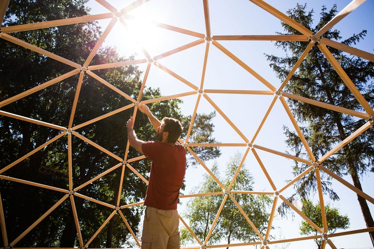 Mann montiert Holzkuppel vor Baumkulisse