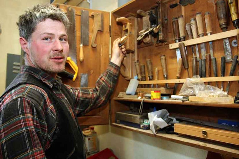 Armoire à outils contenant divers outils tels que rabots, scies et burins, présentée par un homme