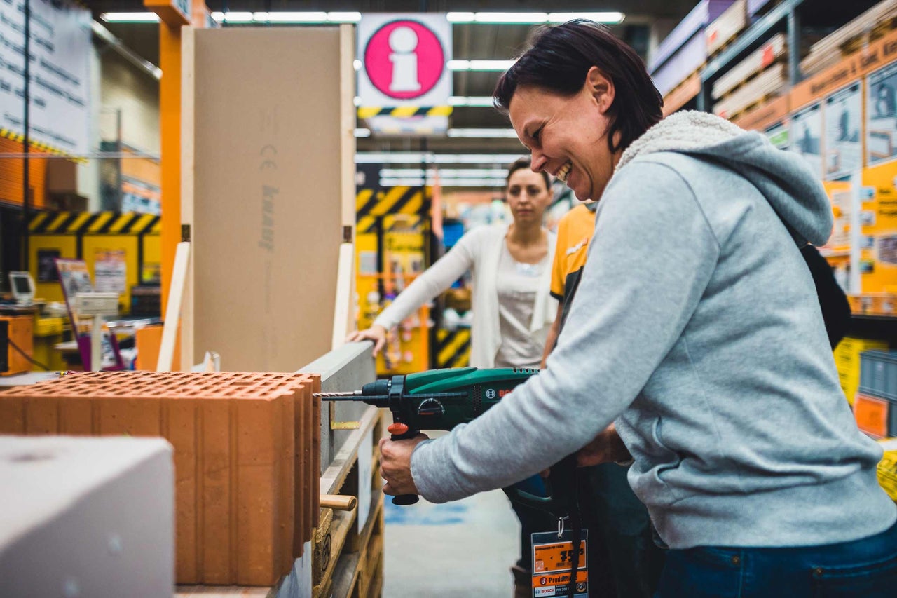 Eine Frau bohrt mit einer Bohrmaschine einen Ziegelstein in einem Hornbach Markt.