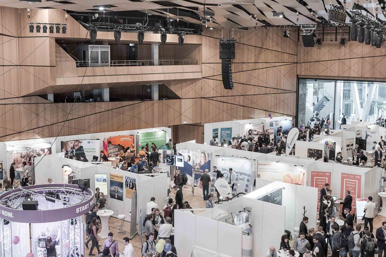 Übersicht einer belebten Messehalle mit verschiedenen Ausstellern und Besuchern.