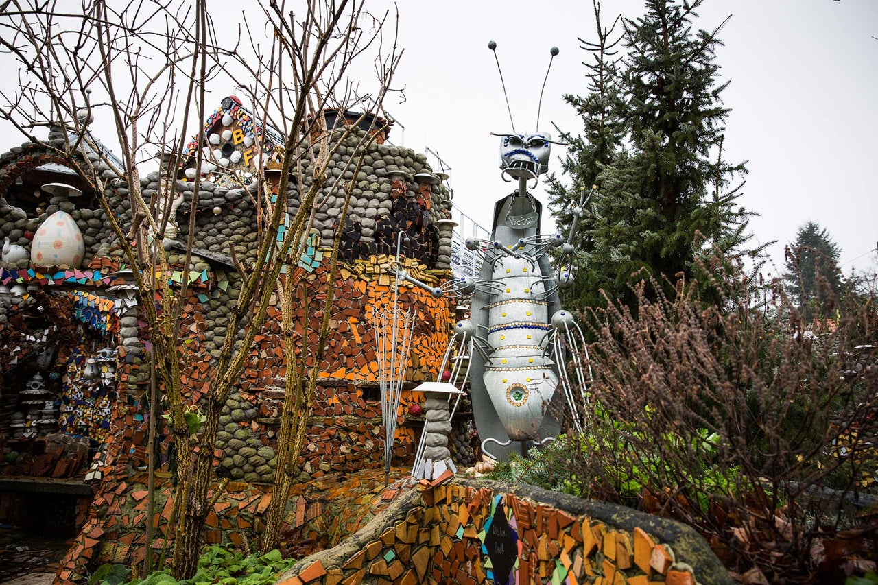 Jardin avec une sculpture d'une figure et une maison avec des décorations de mosaïque.