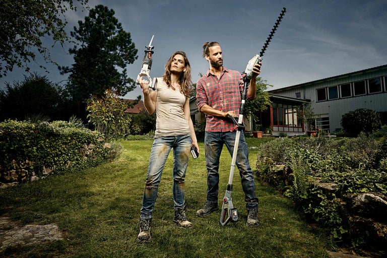 Un homme et une femme se tiennent dans un jardin avec un taille-haie et une scie sabre.