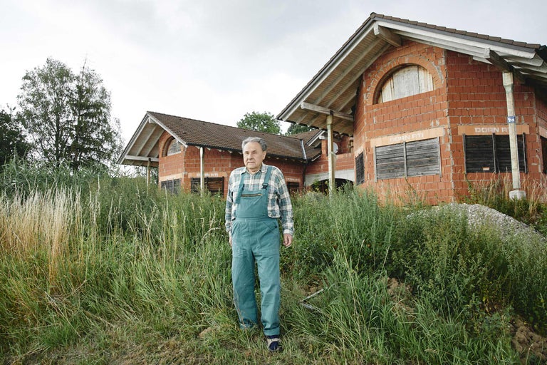 Mann in Arbeitskleidung vor einem Rohbau mit Ziegelmauerwerk