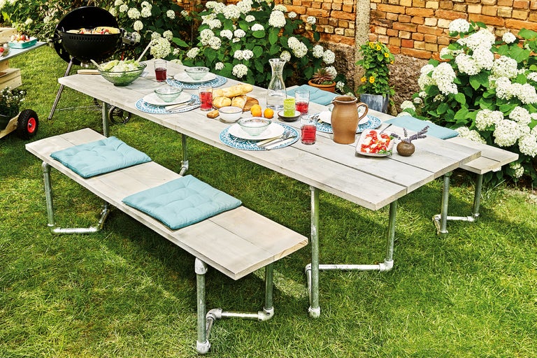Gedeckter Esstisch und Bänke im Garten mit Grill