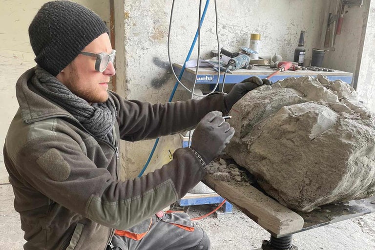 Un tailleur de pierre travaille une pierre avec un outil dans un atelier.