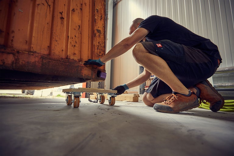 Un homme déplace un conteneur avec un chariot de déménagement dans un hall.
