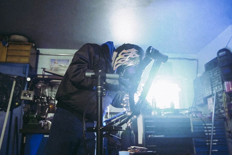 Person schweisst Metall mit Schweisshelm in Werkstatt