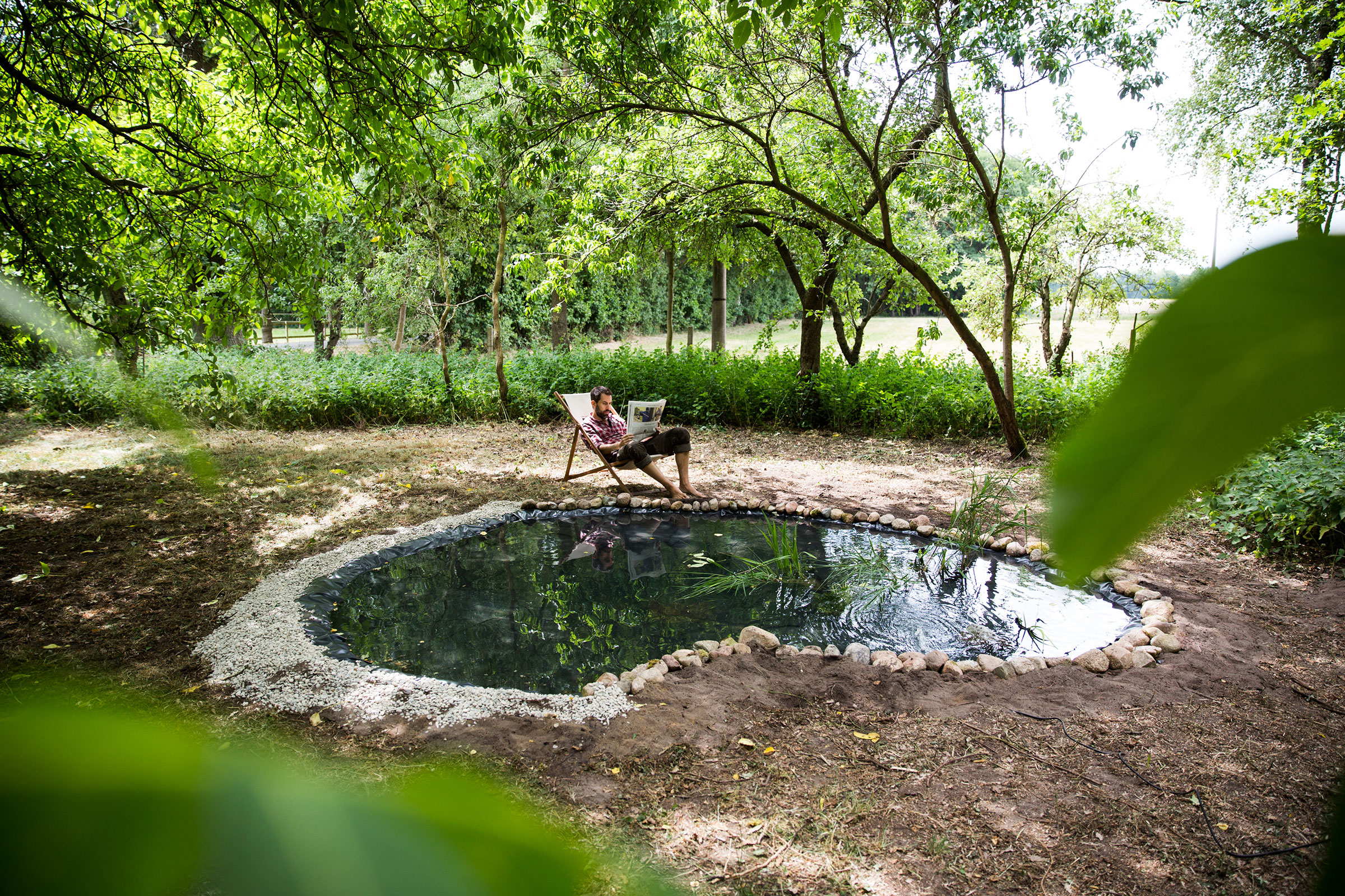 Bassin de jardin avec aménagement de la berge et homme détendu dans un transat