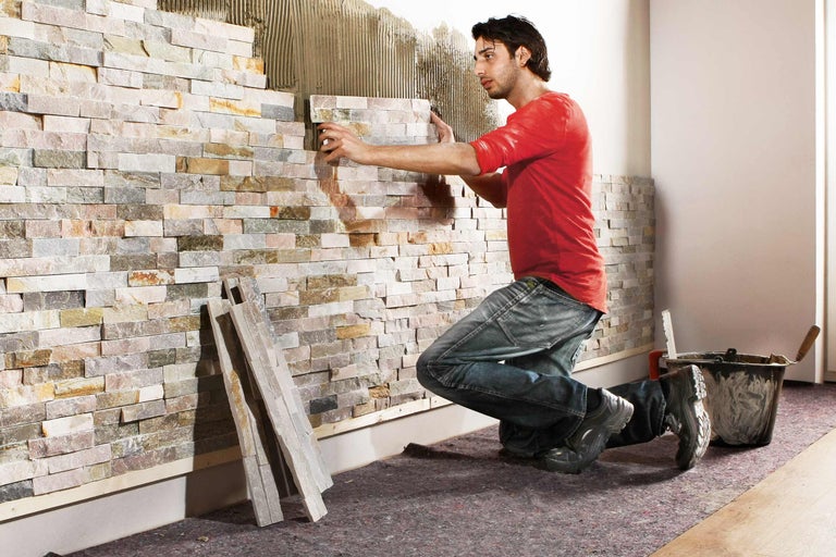Mann verlegt Natursteinverblender an einer Wand im Innenbereich