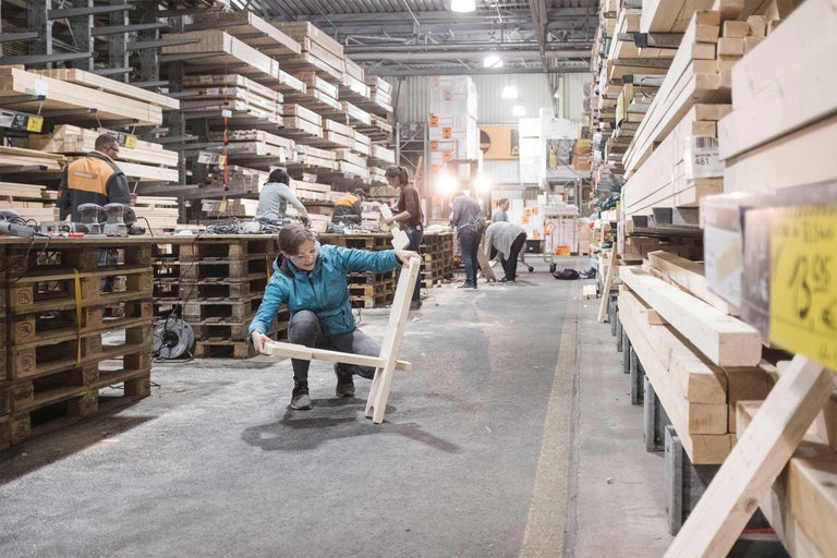 Person baut in einem Baumarkt einen Holzstuhl, im Hintergrund Holzregale