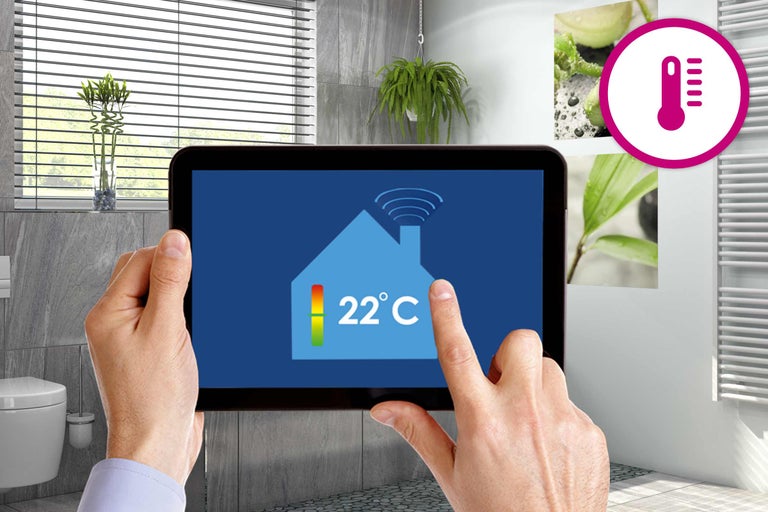 Une personne utilise une tablette dans une salle de bains pour régler la température. Le symbole du thermomètre est visible.