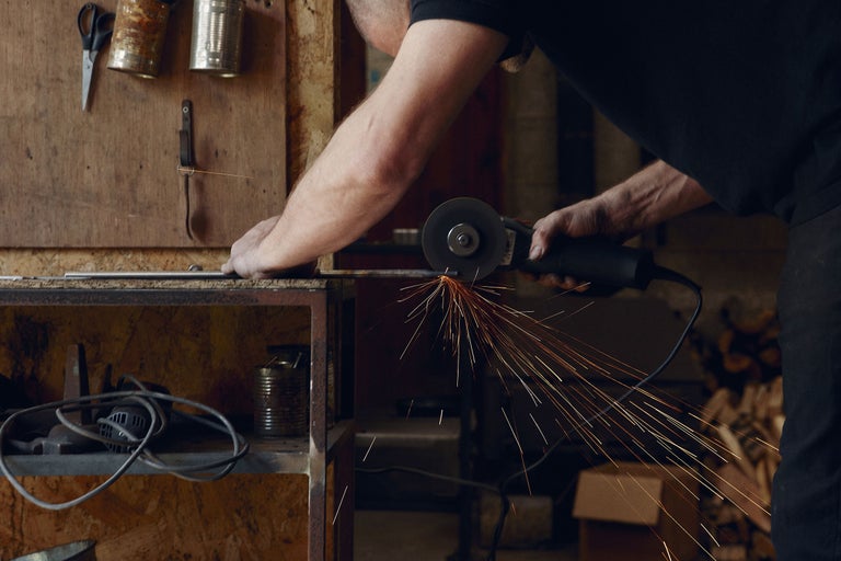 Un homme coupe du métal avec une meuleuse d'angle, produisant des étincelles.