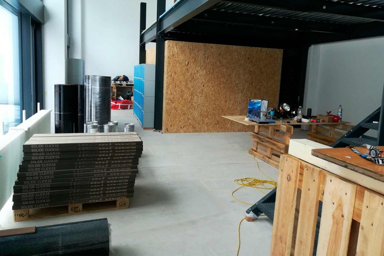 Innenaufnahme eines Raumes mit Baumaterialien wie Bodenplatten, Dämmrollen und Werkzeugen